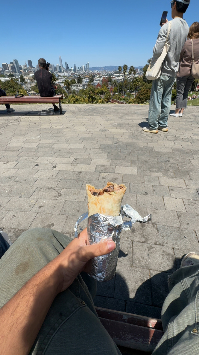 First-person view of a Mission burrito at Dolores Park with the San Francisco skyline in the background